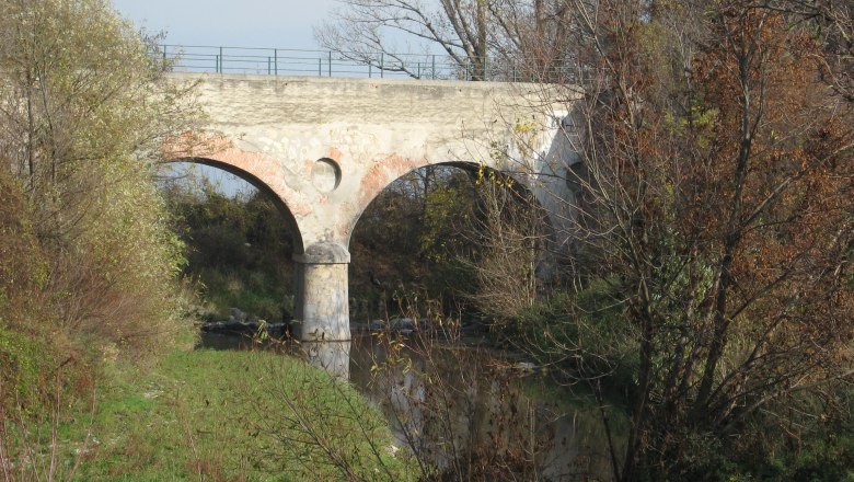 Teesdorf, © Teesdorf Alte Steinbrücke über einen kleinen Fluss, umgeben von Bäumen im Herbst.