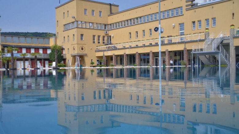 Freibad, © Freizeitzentrum Stadtbad Mödling Ein Freibad mit einem großen gelben Gebäude im Hintergrund, das sich im Wasser spiegelt.