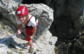 Alpinschule Peilstein, © Alpinschule Peilstein Person klettert an Felsen mit rotem Helm und Seil.