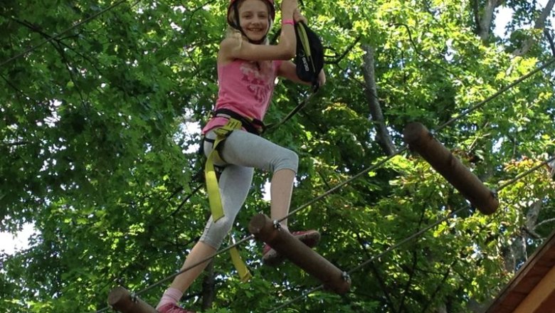 High ropes climbing in Tattendorf, © Soulriders/MB A child wearing a helmet and climbing equipment balances between trees on a high ropes course.