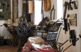 Heimatmuseum, © Heimatmuseum Innenansicht eines Heimatmuseums mit alten Werkzeugen und einem roten Kinderwagen.