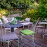 Hotel Landhaus Moserhof, © Niederösterreich Werbung / Maximilian Pawlikowsky Gartenbereich mit Tischen und Stühlen auf Holzterrasse, umgeben von grünen Pflanzen.