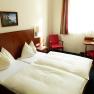 Hotelzimmer neu, © martina krug Ein Hotelzimmer mit zwei Einzelbetten, roten Stühlen und einem kleinen Tisch am Fenster.