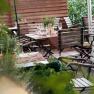 Guest garden, © Babenbergerhof A cozy guest garden with wooden tables and chairs, set with glasses and cutlery, surrounded by plants.