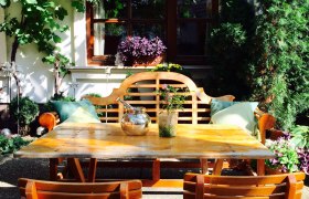 Heurigen Schwertführer, © Schwertführer Gemütlicher Gartenbereich mit Holztisch und Stühlen, umgeben von Pflanzen und Weinreben.