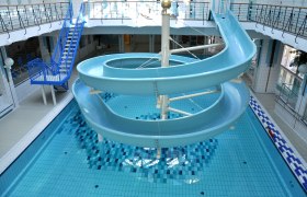 Hallenbad, © Freizeitzentrum Stadtbad Mödling Innenansicht eines Hallenbads mit blauer Wasserrutsche und Schwimmbecken.