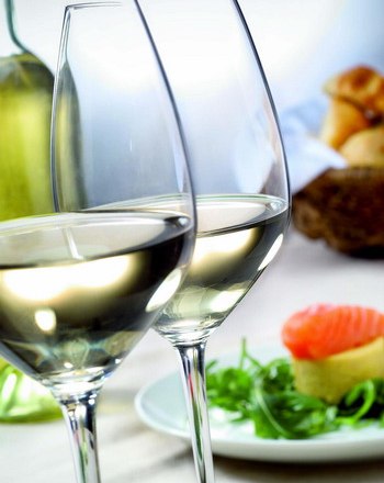 Weingläser, © Weingut Schlösinger Zwei gefüllte Weingläser mit Weißwein, im Hintergrund ein Teller mit Lachs und Salat.