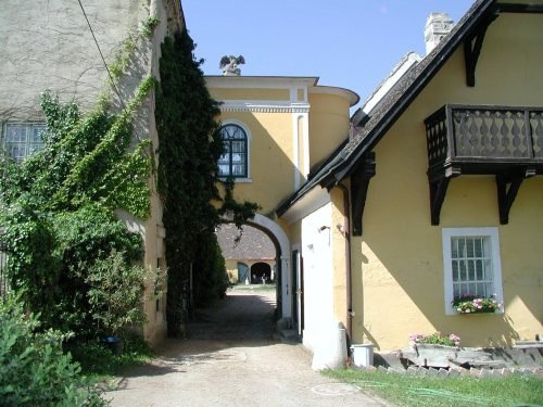 Herzlich Willkommen!, © rgf Ein gelbes Gebäude mit einem Torbogen, umgeben von Efeu und einem kleinen Balkon.
