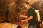 A man in a wine cellar checks the contents of a wine barrel.