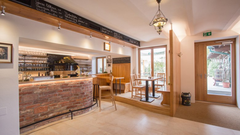 Interior view of a cozy wine bar with wooden furniture and brick counter.
