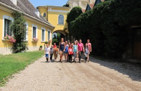Gruppe von Kindern und Erwachsenen mit Pony vor gelbem Geb&auml;ude.