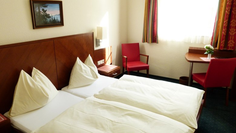 Ein Hotelzimmer mit zwei Einzelbetten, roten Stühlen und einem kleinen Tisch am Fenster.
