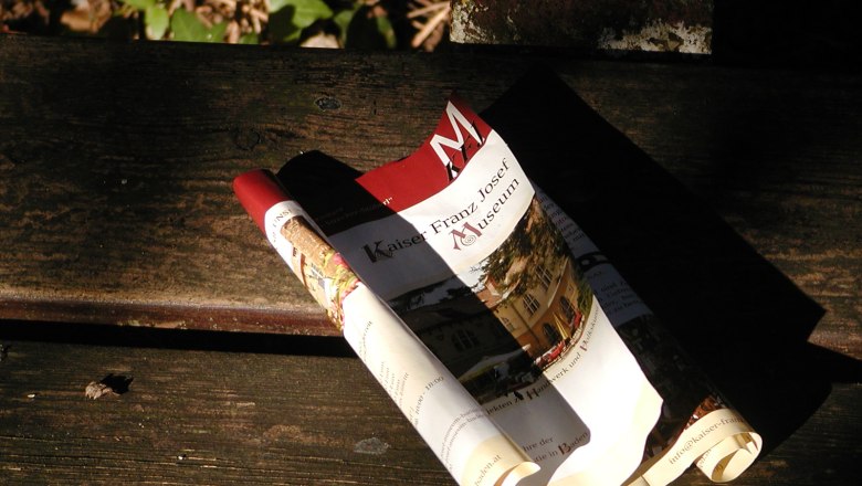 Rolled up brochure of the Kaiser-Franz-Josef-Museum on a wooden bench.