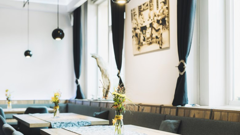Interior view of a stylish café with wooden tables, flower vases and black curtains.