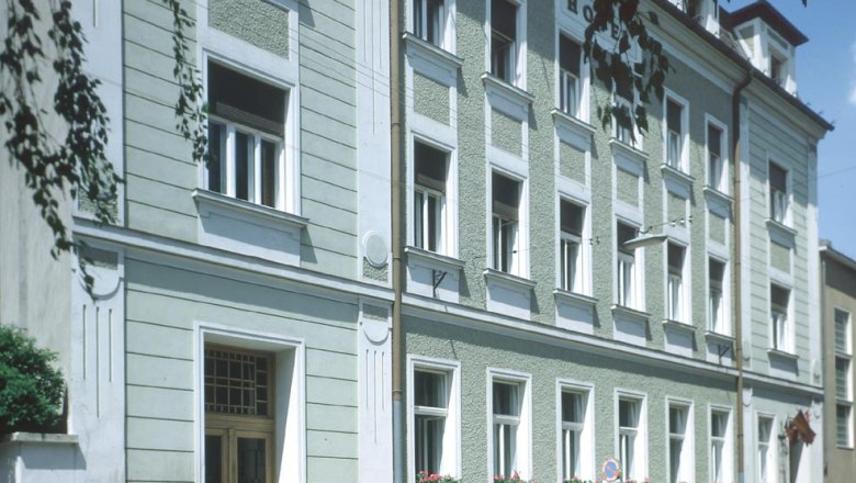 Außenansicht eines mehrstöckigen Gebäudes mit grüner Fassade und weißen Fensterrahmen.