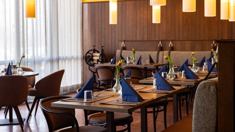 Ein stilvoll eingerichtetes Restaurant mit gedeckten Tischen, blauen Servietten und Tulpen in Vasen.