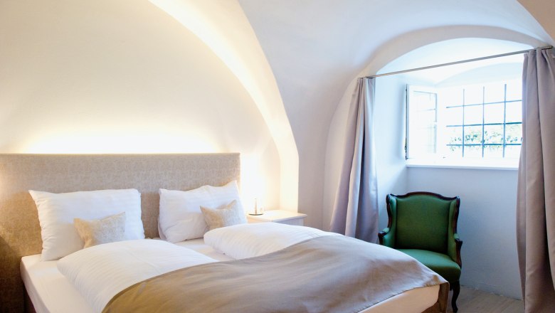 Gem&uuml;tliches Schlafzimmer mit Doppelbett, gr&uuml;nem Sessel und gew&ouml;lbter Decke.