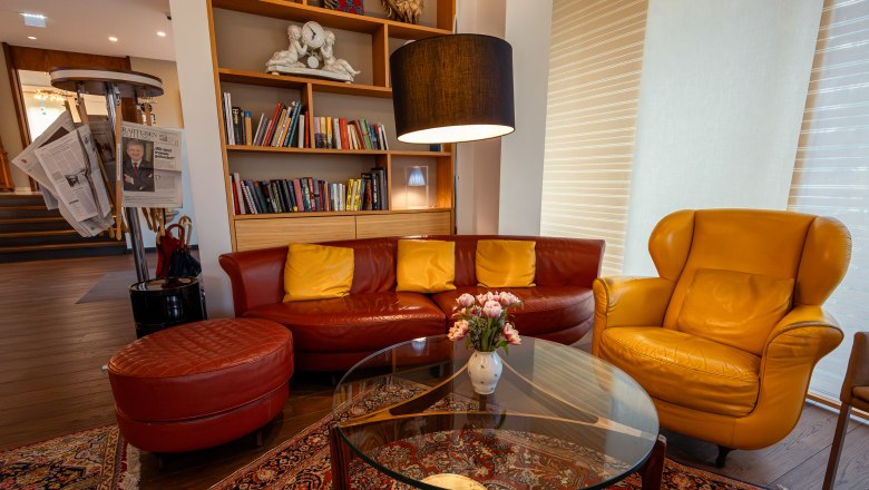 Cozy hotel lobby with red and yellow leather furniture, bookshelf and newspaper rack.