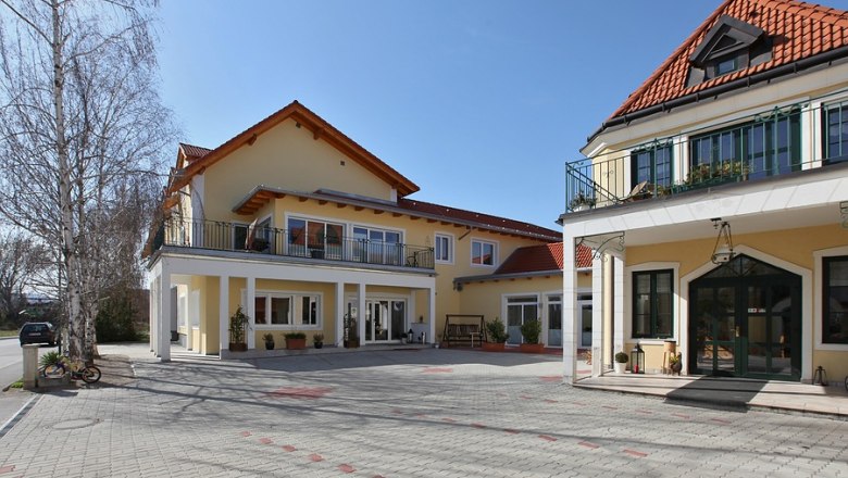 Außenansicht eines gelben Winzerhofs mit roten Dächern und gepflastertem Hof.