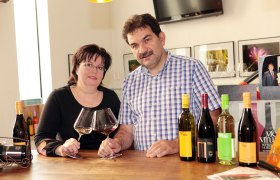 Ein Mann und eine Frau stehen an einem Tisch mit Weingl&auml;sern und Weinflaschen.