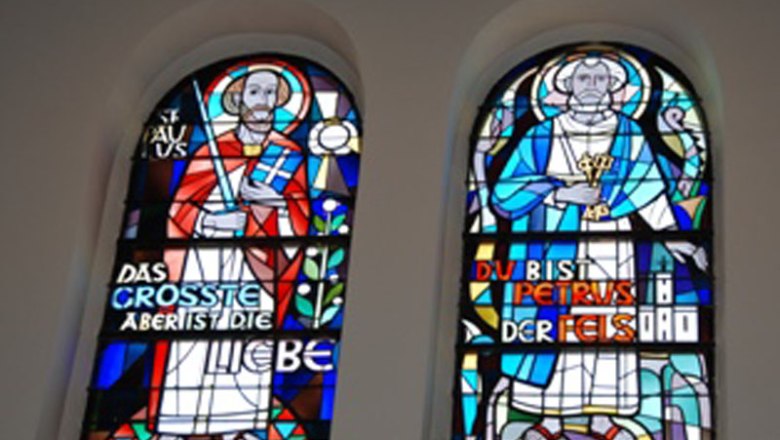 Zwei bunte Kirchenfenster mit religi&ouml;sen Figuren und Inschriften.