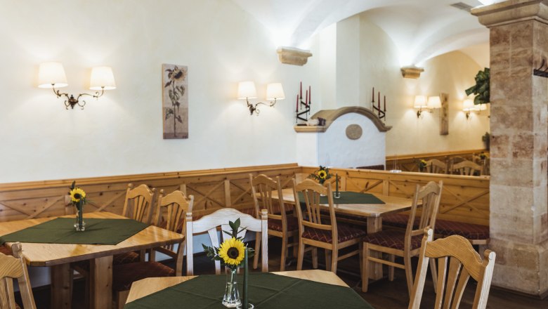 Gem&uuml;tliche Wirtshausstube mit Holzm&ouml;beln, gr&uuml;nen Tischdecken und Sonnenblumen in Vasen.