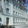 Außenansicht eines mehrstöckigen Gebäudes mit grüner Fassade und weißen Fensterrahmen.