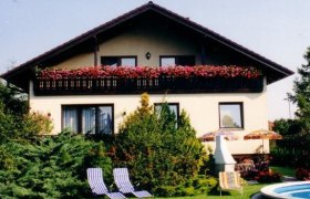 Zweistöckiges Haus mit Balkon, Gartenmöbeln und Pool im Vordergrund.