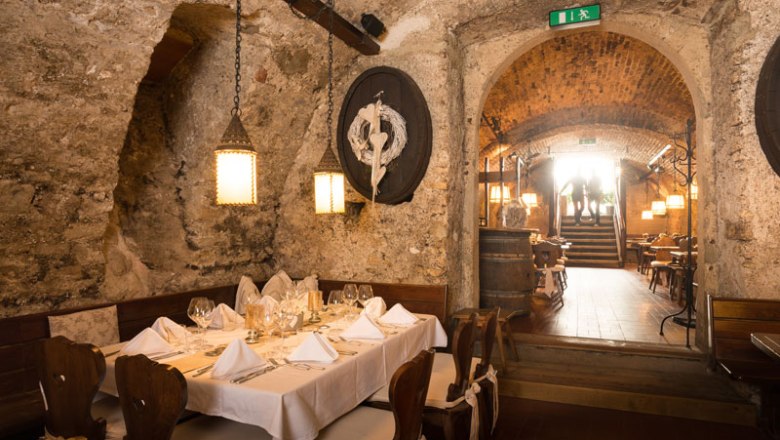 Ein rustikales Kellerrestaurant mit gedecktem Tisch, Steinwänden und Holzmöbeln.