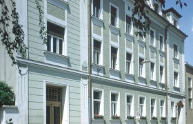 Au&szlig;enansicht eines mehrst&ouml;ckigen Geb&auml;udes mit gr&uuml;ner Fassade und wei&szlig;en Fensterrahmen.