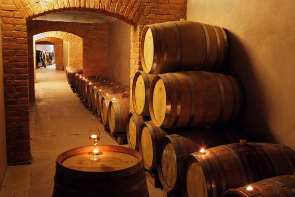 Ein Weinkeller mit gestapelten Holzfässern und einem Glas Wein auf einem Fass.