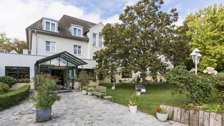 Eingang der Holdrichsmühle mit Garten und Bäumen.