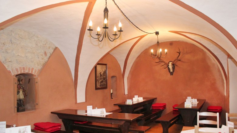 Rustikales Restaurant mit Gewölbedecke, Holztischen und Hirschgeweih an der Wand.