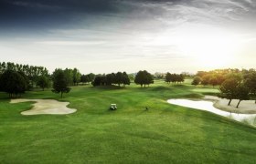 Golfplatz mit grünen Fairways, Sandbunkern und einem Golfwagen bei Sonnenuntergang.