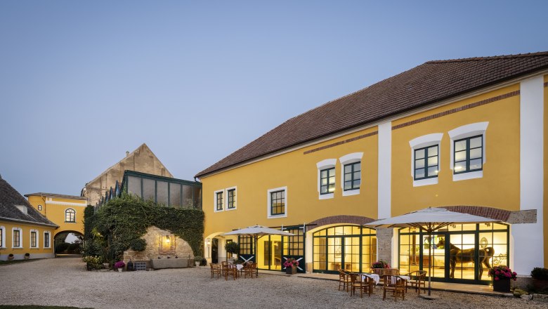 Yellow building with courtyard and outdoor tables at dusk.