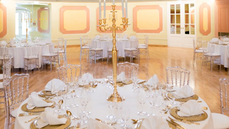 Eleganter Theatersaal mit runden, festlich gedeckten Tischen und goldenen Kerzenhaltern.