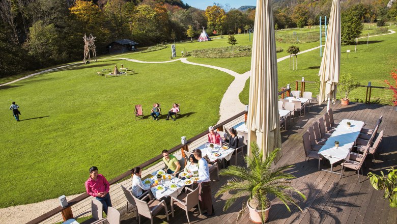 Terrace of the Krainerhütte seminar and event hotel with guests eating, surrounded by green meadows and forest.