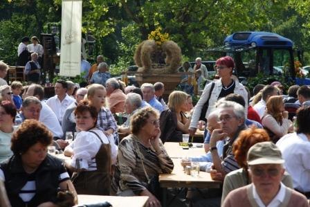 Menschen sitzen bei einem Fest im Freien an Holztischen.