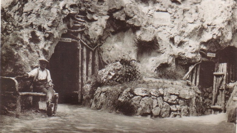Historisches Foto der Einödhöhle in Pfaffstätten, Baden, mit einem Mann auf einer Bank vor dem Höhleneingang.