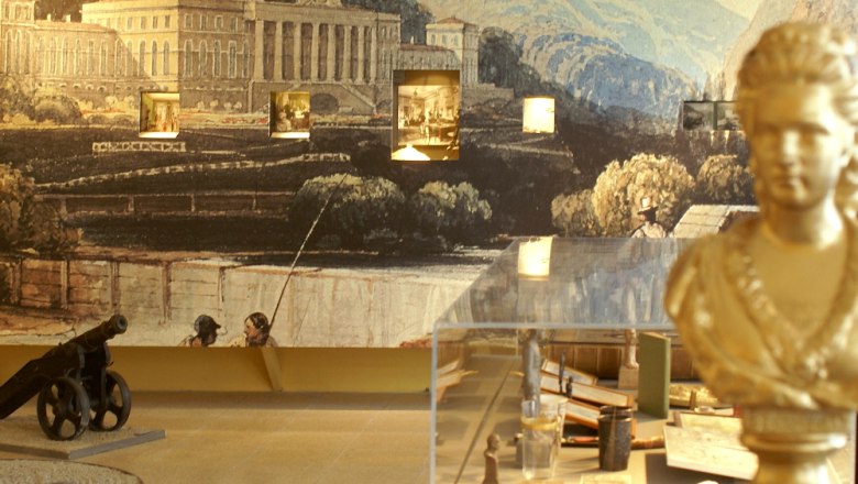 Interior view of a museum with bust, cannon and mural.