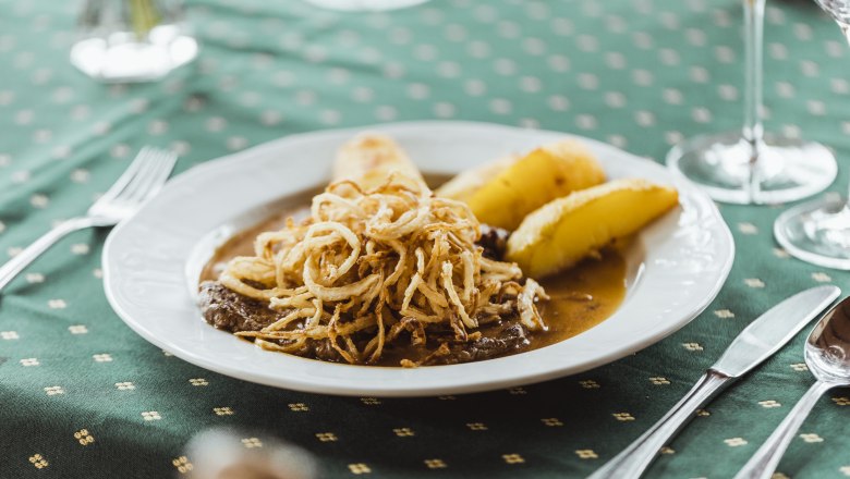 Ein Teller mit Zwiebelrostbraten und Braterd&auml;pfeln auf einem gr&uuml;nen Tisch.