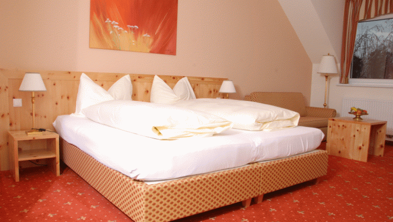 Gem&uuml;tliches Hotelzimmer mit Doppelbett, Holzm&ouml;beln und rotem Teppich.