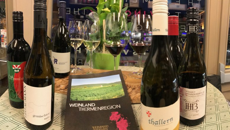 Wine bottles and glasses on a table with a brochure of the Thermenregion wine region.