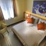 Cozy hotel room with a double bed, two orange pillows, a desk, an armchair and a large flower picture on the wall.
