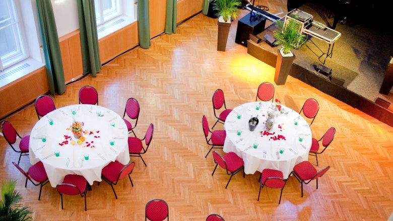 A festively decorated hall with round tables and red chairs, view from above.