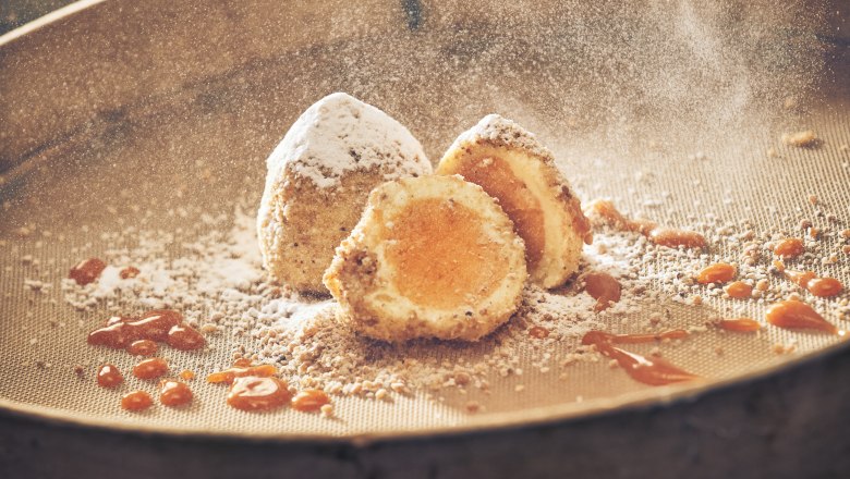 Eismarillenknödel mit Puderzucker und Aprikosensauce auf einem Sieb.