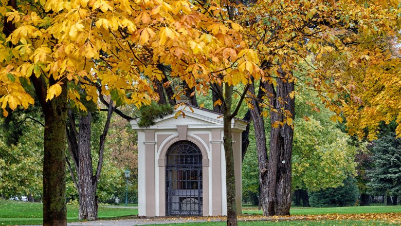 Ein kleines Gebäude in einem Park, umgeben von Bäumen mit gelbem Herbstlaub.