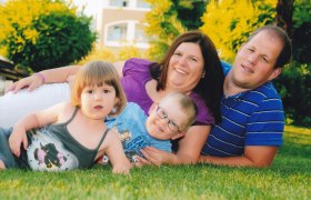 Eine Familie liegt lächelnd auf einer Wiese, bestehend aus zwei Erwachsenen und zwei Kindern.