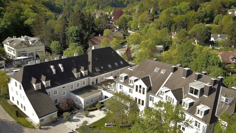 Aerial view of a large building complex surrounded by green trees and hills.
