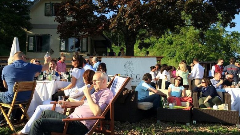 Menschen entspannen bei einer Gartenparty vor einem Haus mit Bäumen.